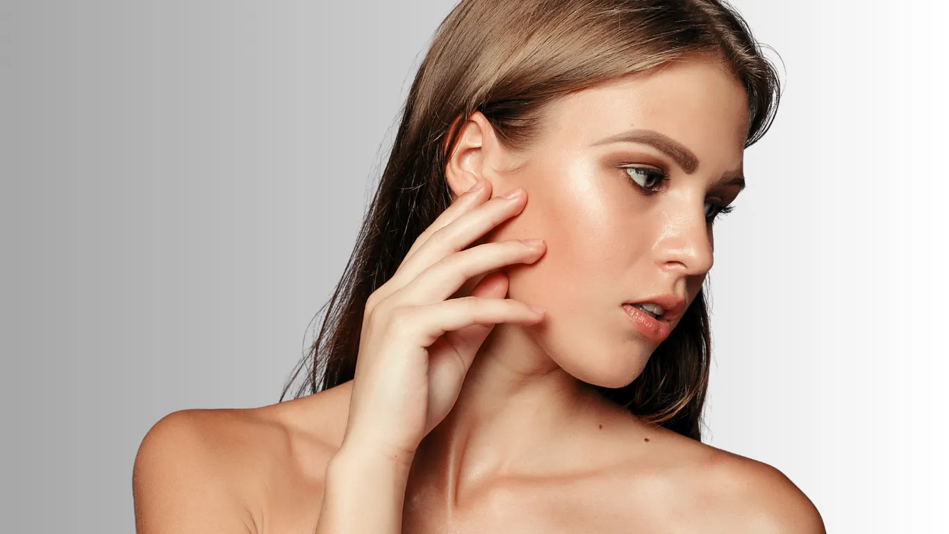 Woman with hand touching her cheek and ear, side profile, against a gray background
